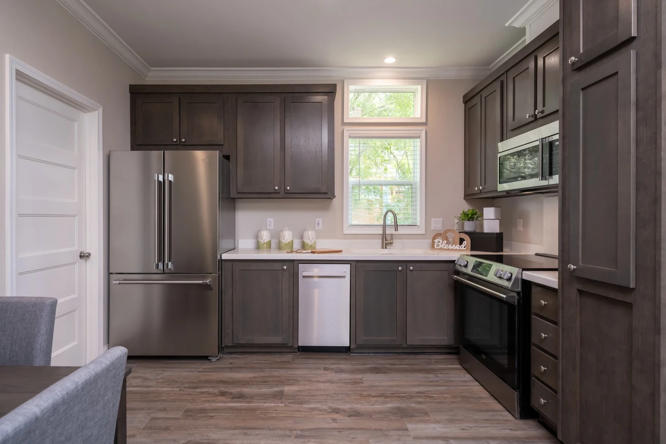 Modern kitchen with dark wood cabinets, stainless steel appliances, a white countertop, and a window above the sink letting in natural light.