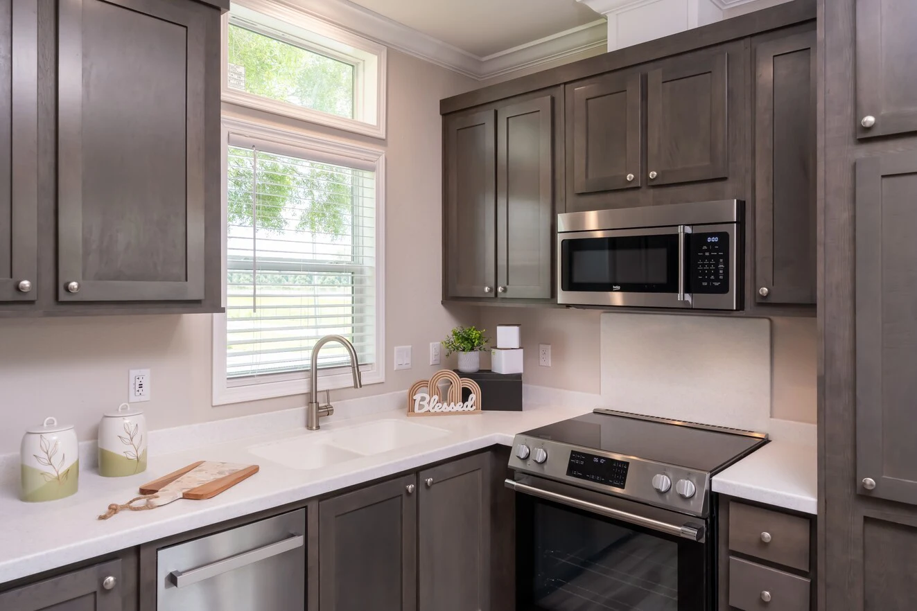 Modern kitchen with gray cabinets, stainless steel appliances, a white sink, and countertop decor including containers and a "Blessed" sign near the window.
