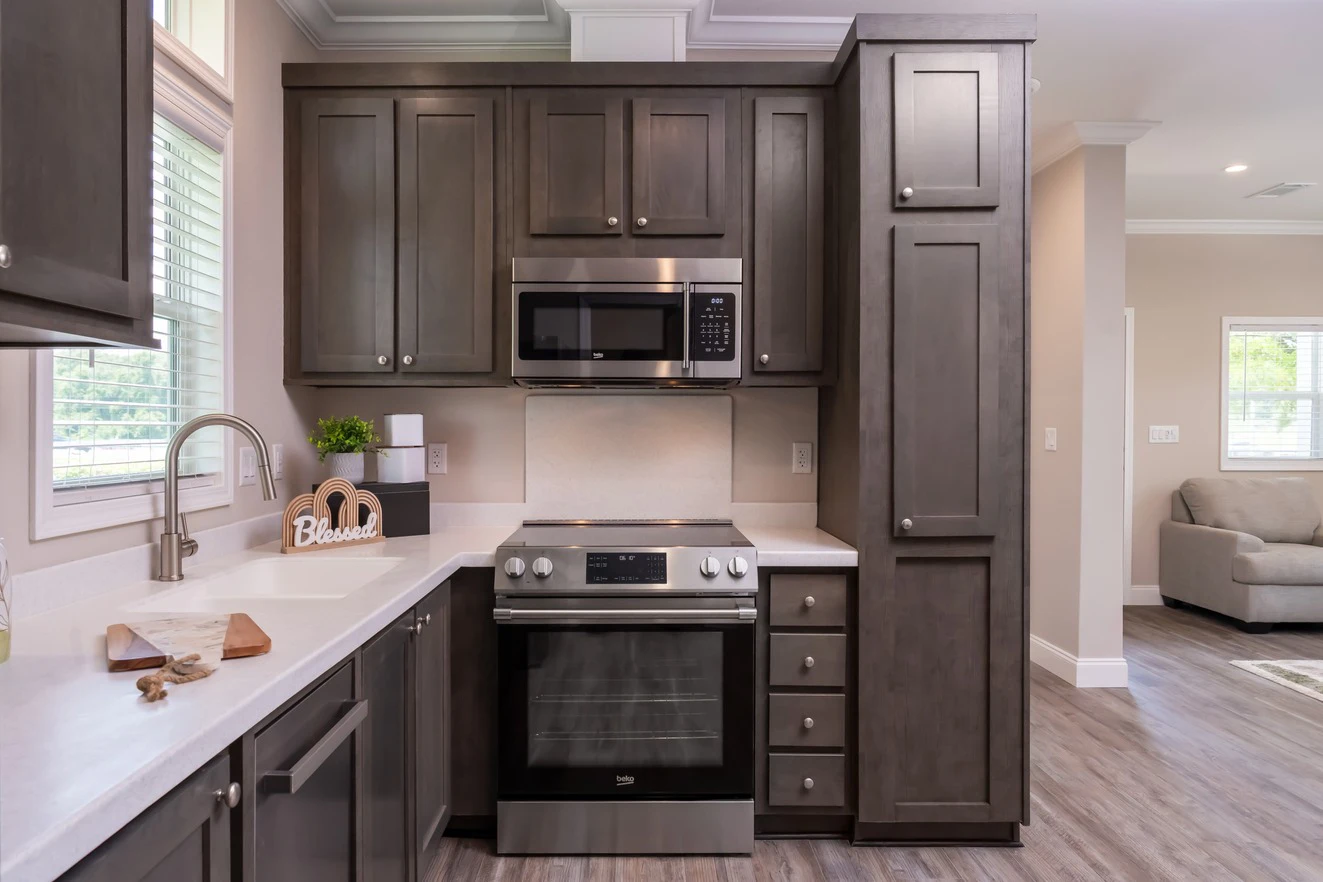 Modern kitchen with dark wood cabinets, stainless steel oven and microwave, white countertops, and a window above the sink.