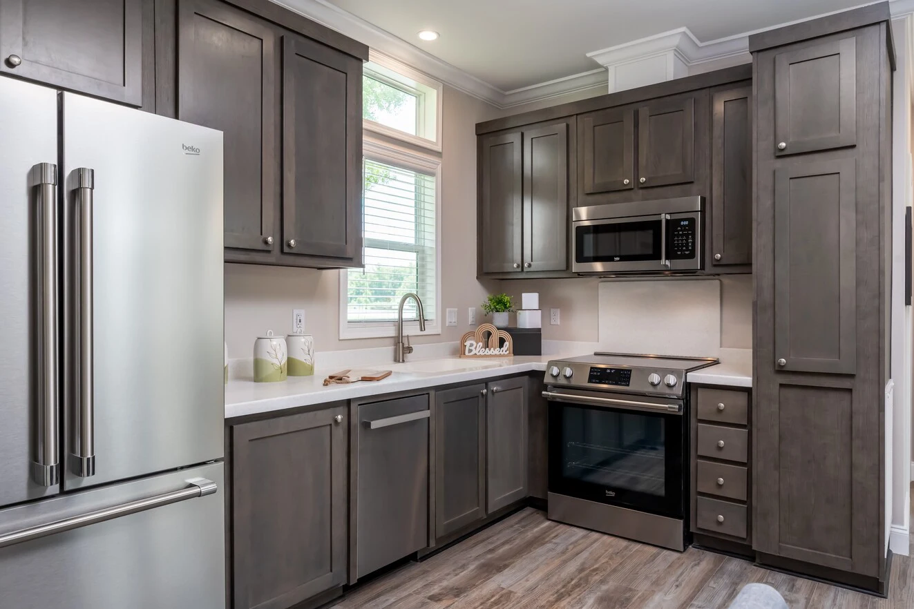 Modern kitchen with gray cabinets, stainless steel appliances, wood flooring, a window above the sink, and a "Blessed" sign on the counter.