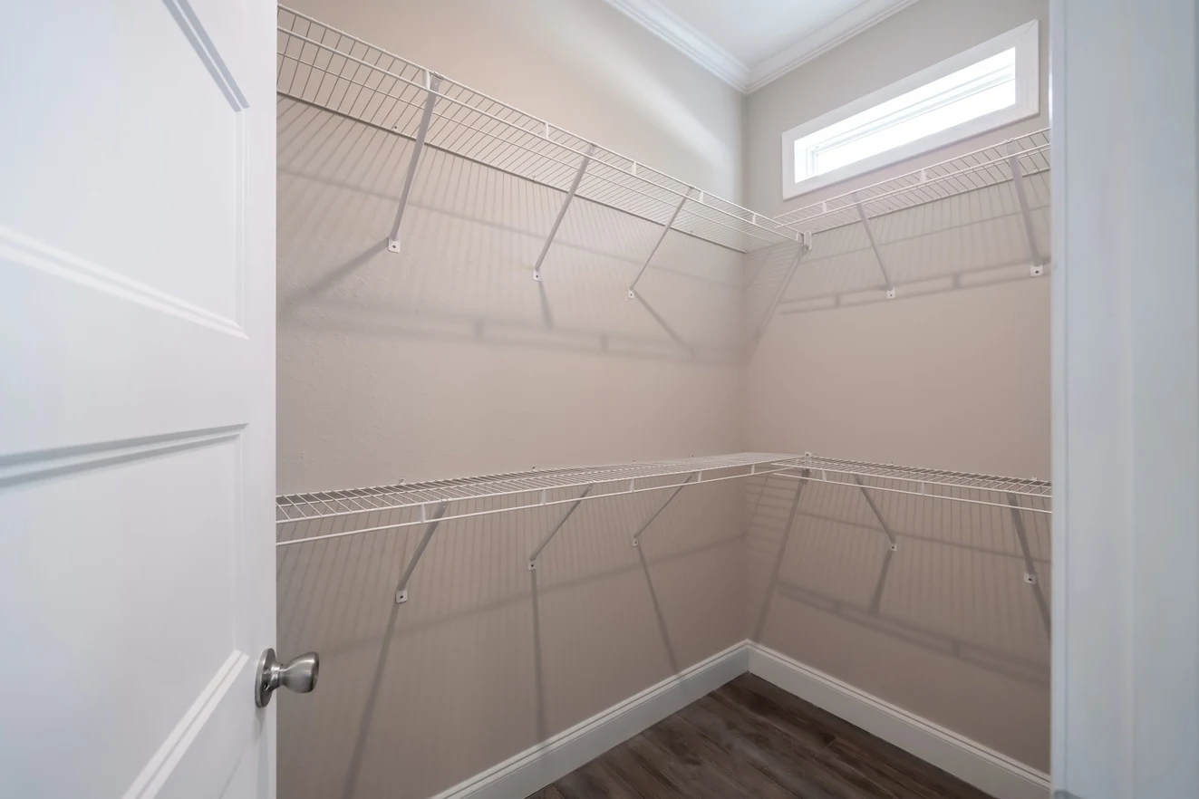 Empty walk-in closet with beige walls, white wire shelving on two sides, a small upper window, and wood-look flooring.