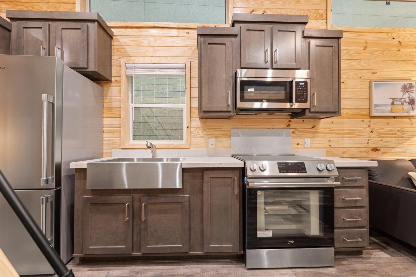 Modern kitchen with stainless steel appliances, farmhouse sink, gray cabinets, electric stove, microwave, and light wood-paneled walls.