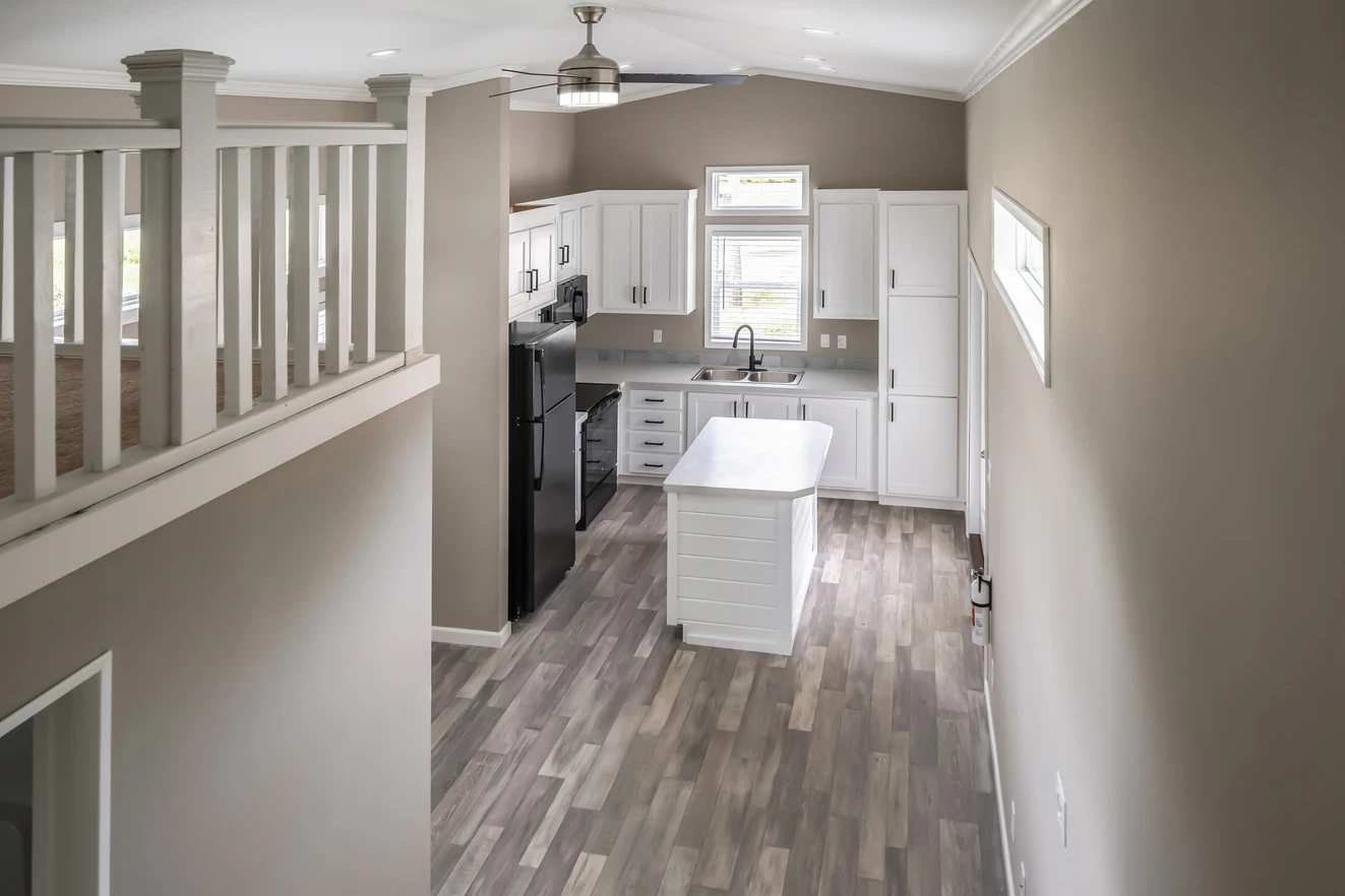 Modern kitchen with white cabinets, a center island, black appliances, and wood-look flooring viewed from an upper level balcony.