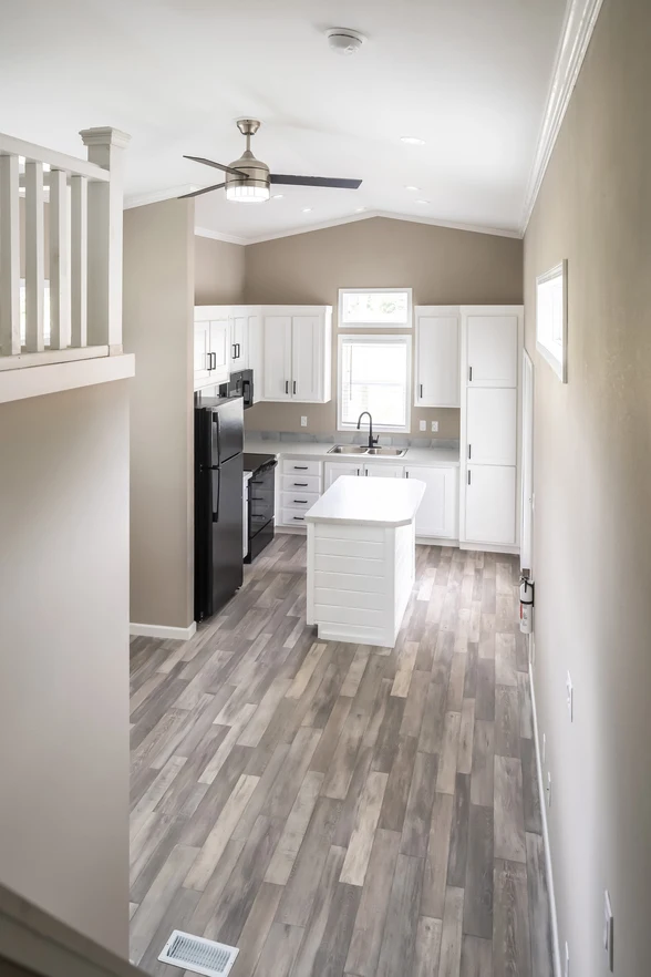 Modern kitchen with white cabinets, black appliances, a small central island, wood-look flooring, and neutral-colored walls, viewed from an elevated angle.