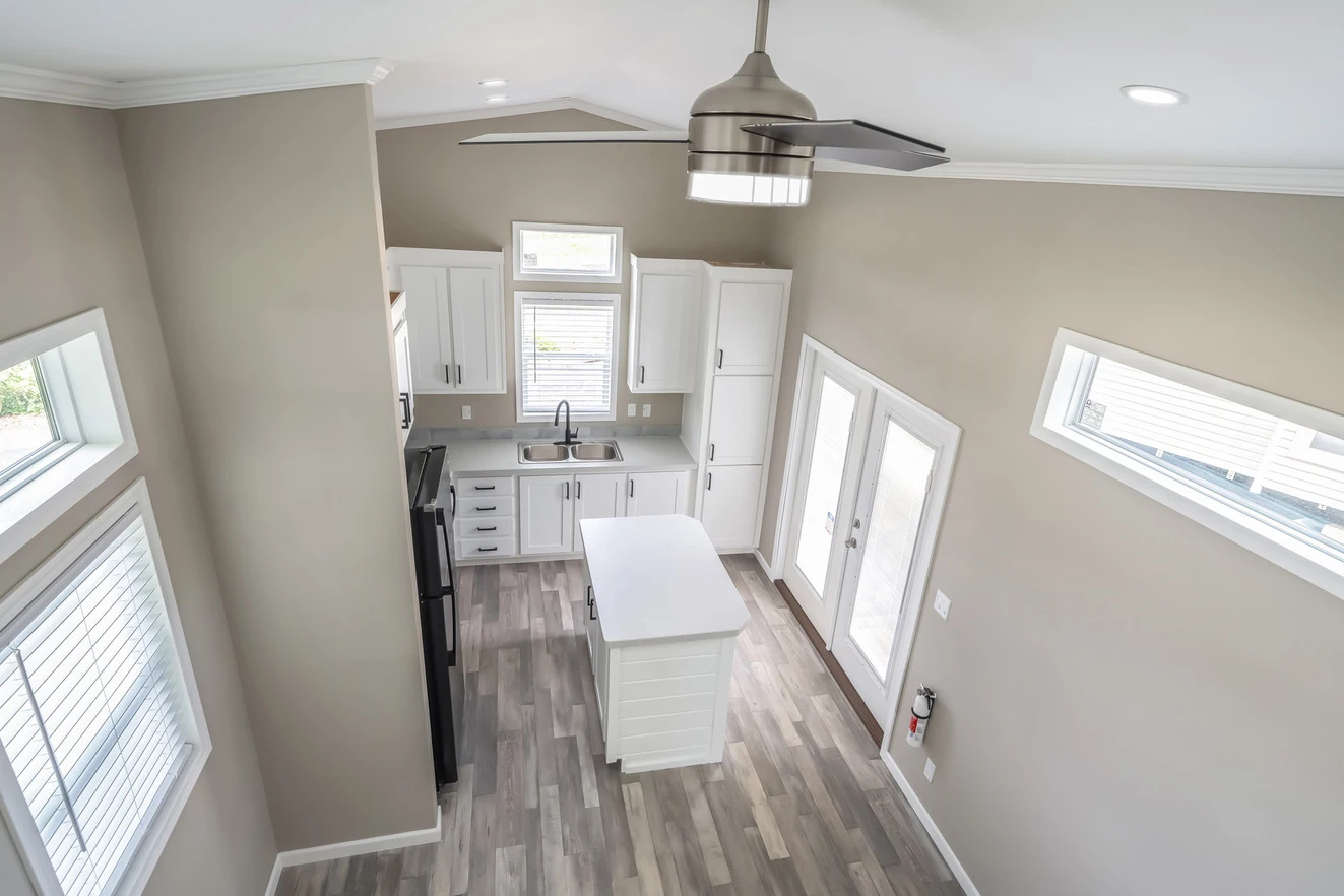 Modern kitchen with white cabinets, center island, gray flooring, stainless steel appliances, and large windows, viewed from above.