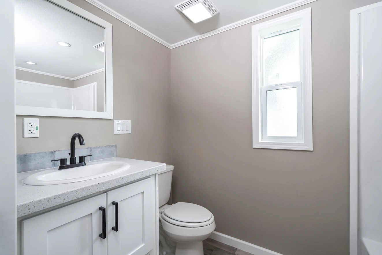 Bathroom with a white vanity, black faucet, wall mirror, toilet, and a frosted window on a beige wall.