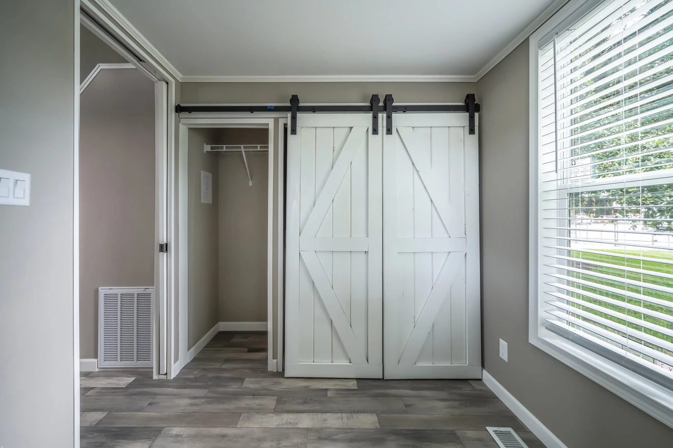 Empty room with gray walls, wood-look flooring, a large window with blinds, and a closet with white barn-style sliding doors.