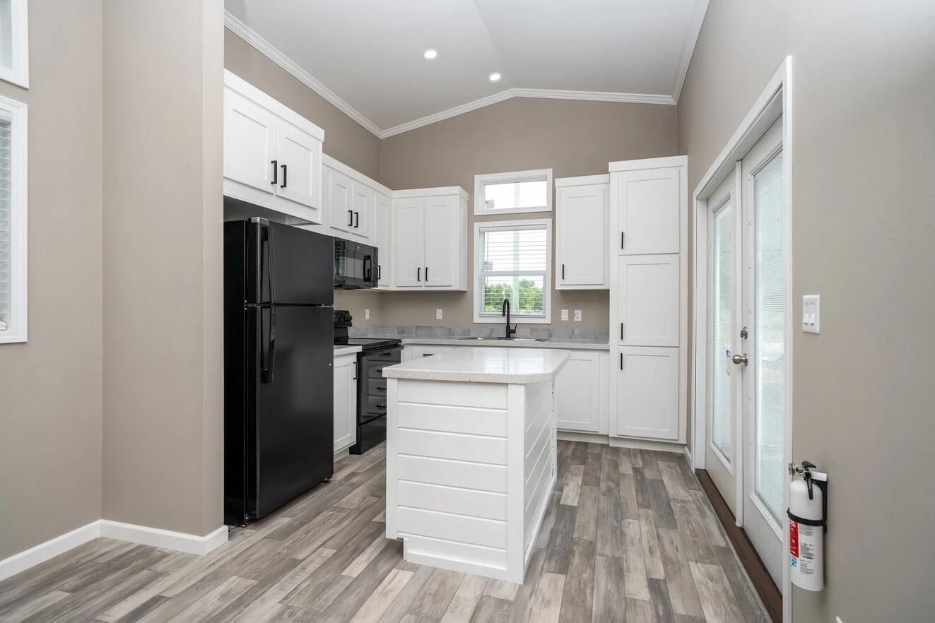 Modern kitchen with white cabinets, black appliances, center island, wood-style flooring, large windows, and a glass door; a fire extinguisher is mounted by the door.
