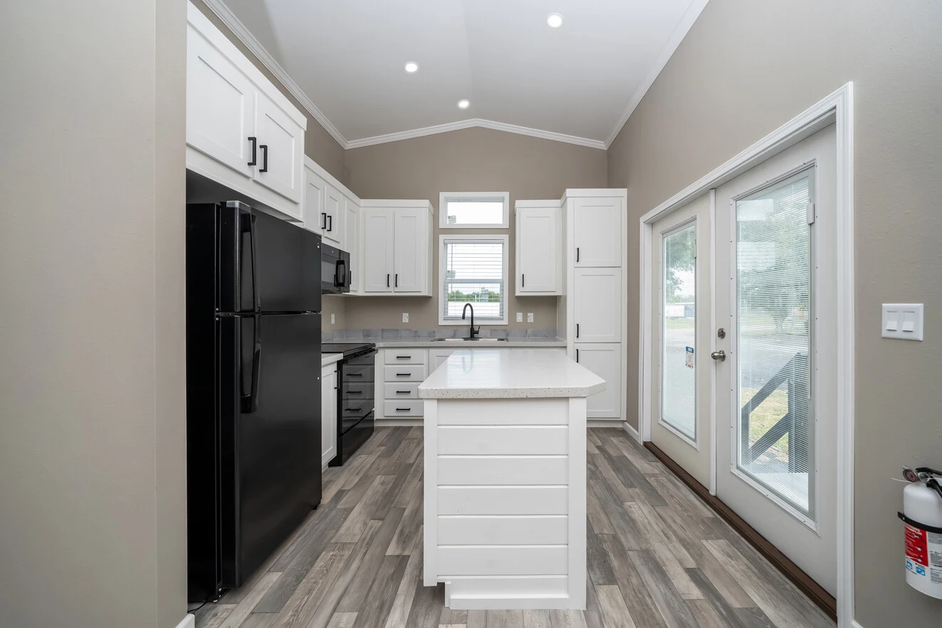 Modern kitchen with white cabinets, black appliances, a center island, wood-look flooring, and glass double doors leading outside. A fire extinguisher is mounted on the wall near the door.