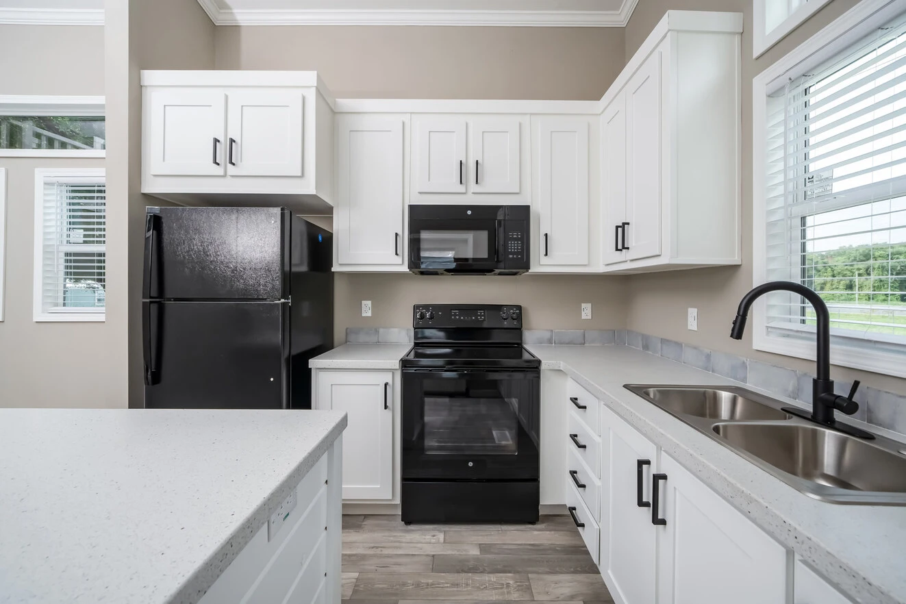 Modern kitchen with white cabinets, black appliances, double sink, light countertops, and large windows providing natural light.