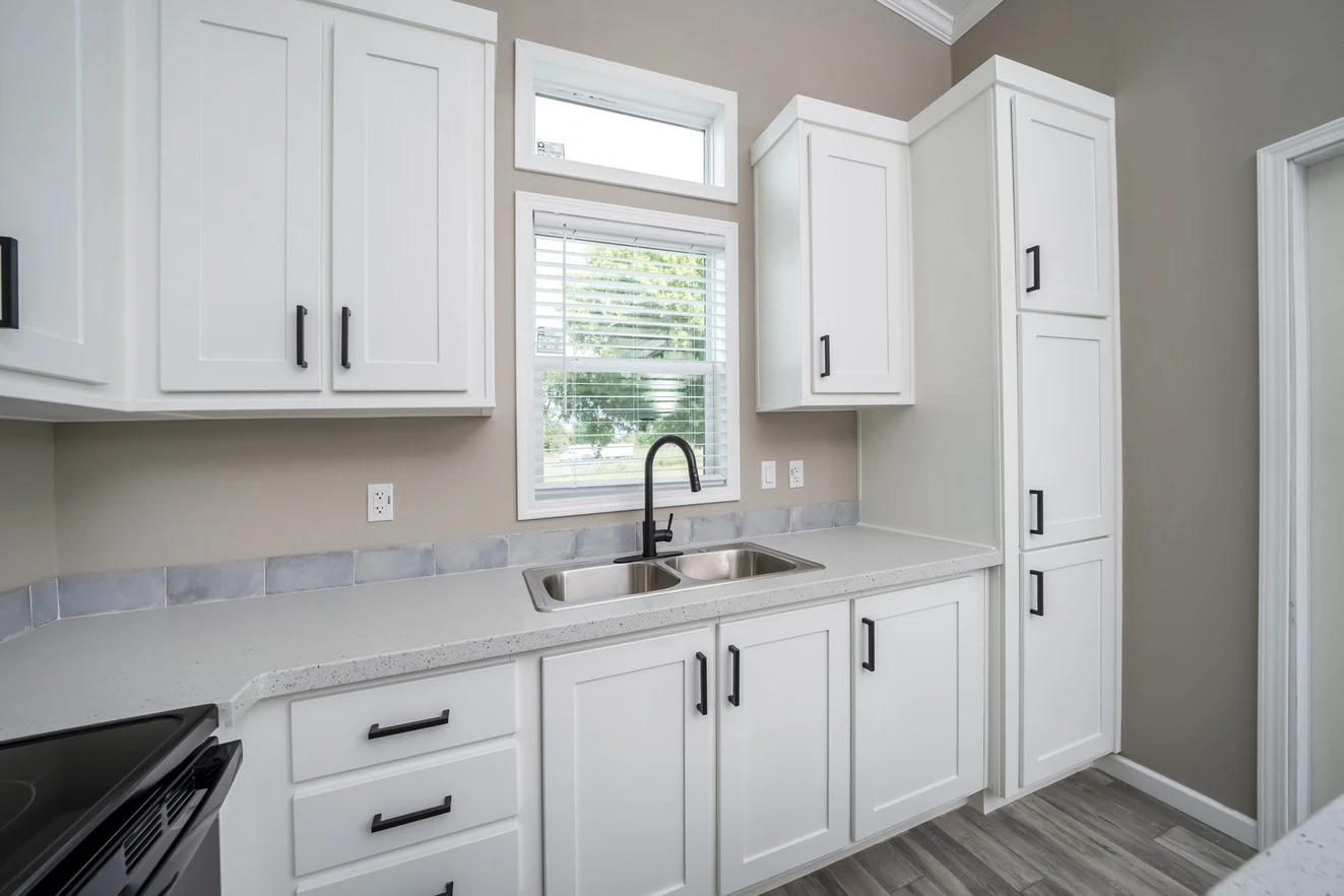 Modern kitchen with white cabinets, black handles, a double sink with a black faucet, a window above the sink, and light-colored countertops and flooring.