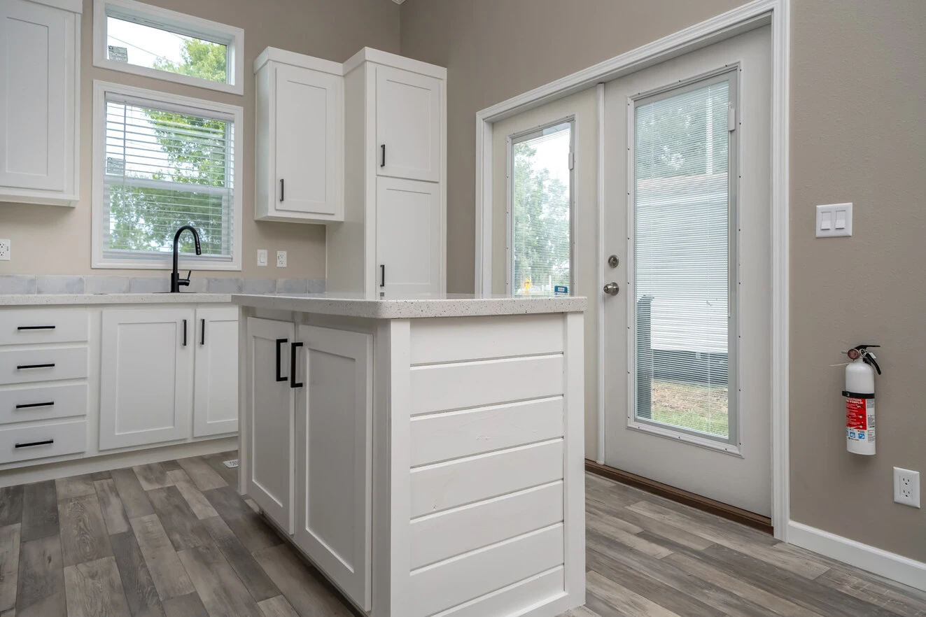 Modern kitchen with white cabinets, an island, large windows, a glass door to the outside, and a fire extinguisher mounted on the wall.