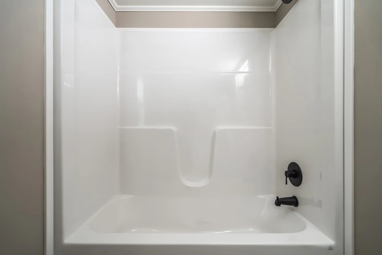 White fiberglass bathtub and shower combo with beige walls, built-in shelves, and black faucet and handle on the right side.
