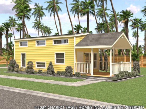 A yellow tiny house with white trim, a front porch, small shrubs, and palm trees in the background. The home sits on a manicured lawn beside a paved road.