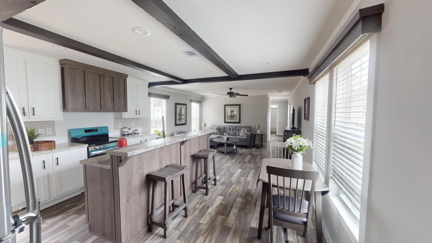Modern open-concept kitchen and living area with wood accents, bar stools, dining table, large windows, and neutral decor.