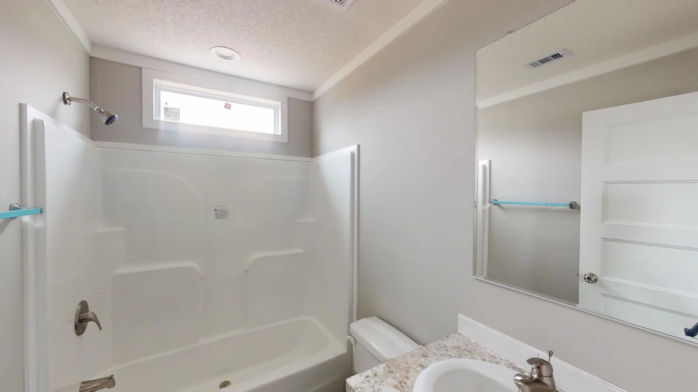 A bathroom with a white bathtub and shower, a toilet, a countertop sink, a wall mirror, and a small window above the tub.