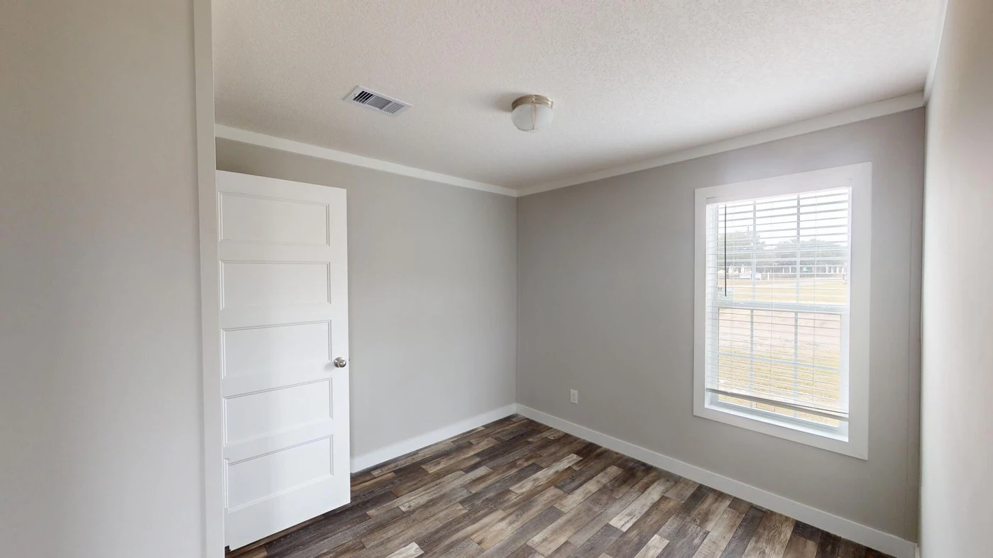 Small empty room with gray walls, white trim, a window with blinds, a white door, and wood-patterned flooring.