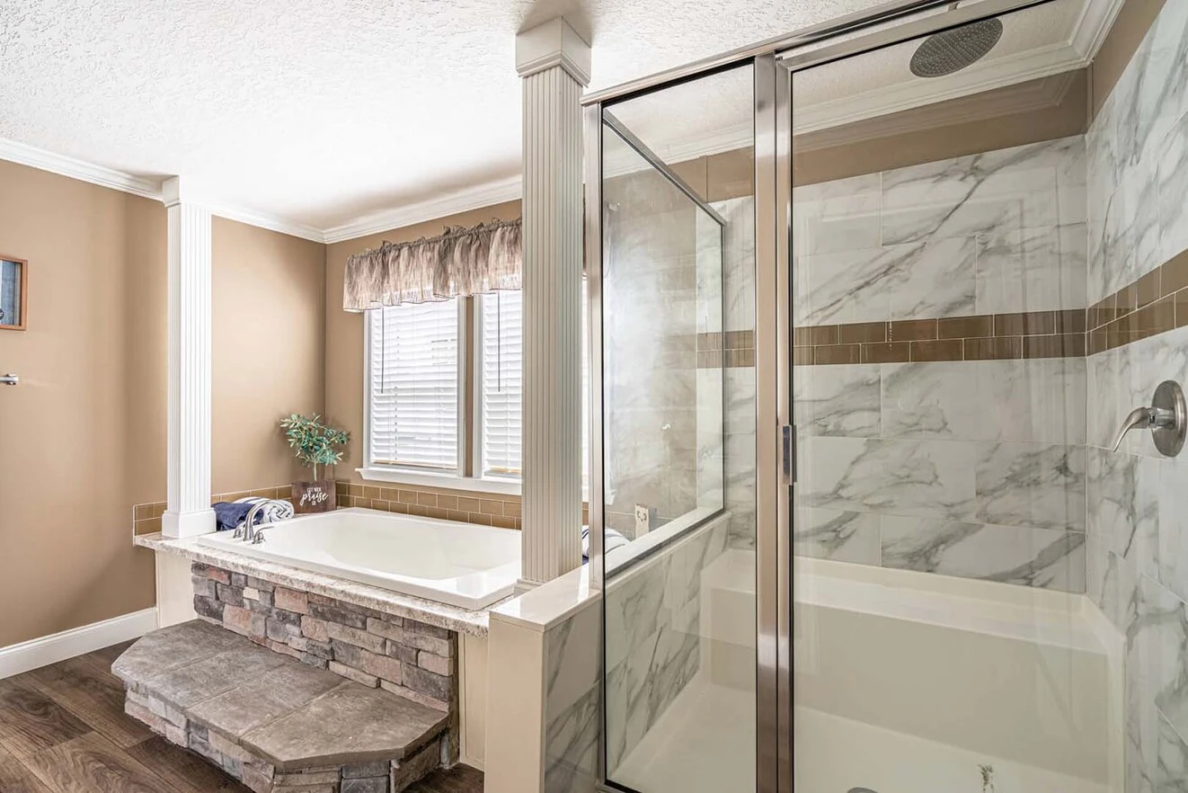 Bathroom with a glass-enclosed shower, a built-in bathtub with stone accents, large window with a valance, and beige walls with white trim.