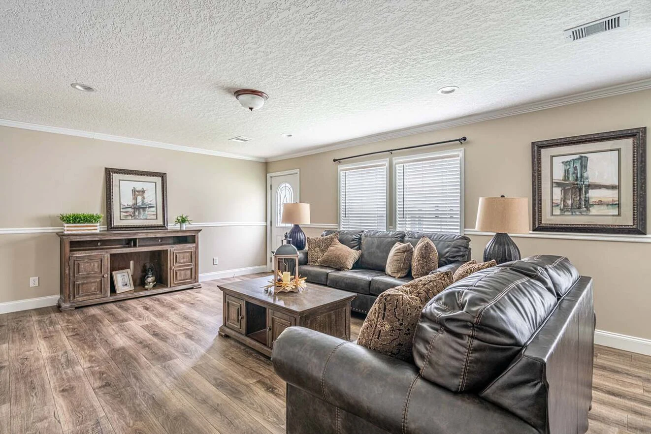 A living room with dark leather sofas, a wooden coffee table, two lamps, framed art on the walls, and a console with decor on a wood floor.