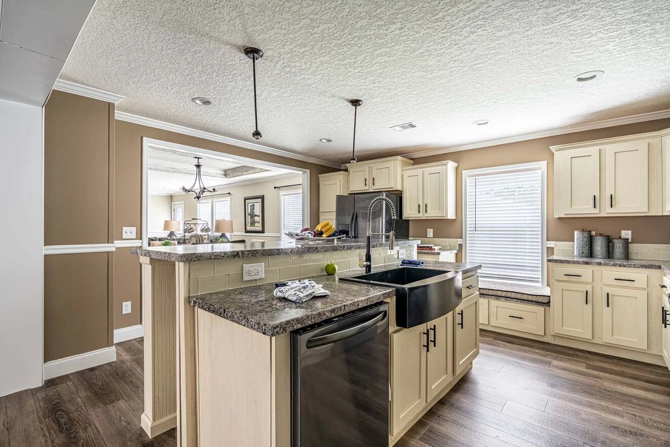 Modern kitchen with beige cabinets, dark countertops, farmhouse sink, stainless appliances, wood flooring, and ample natural light from large windows.