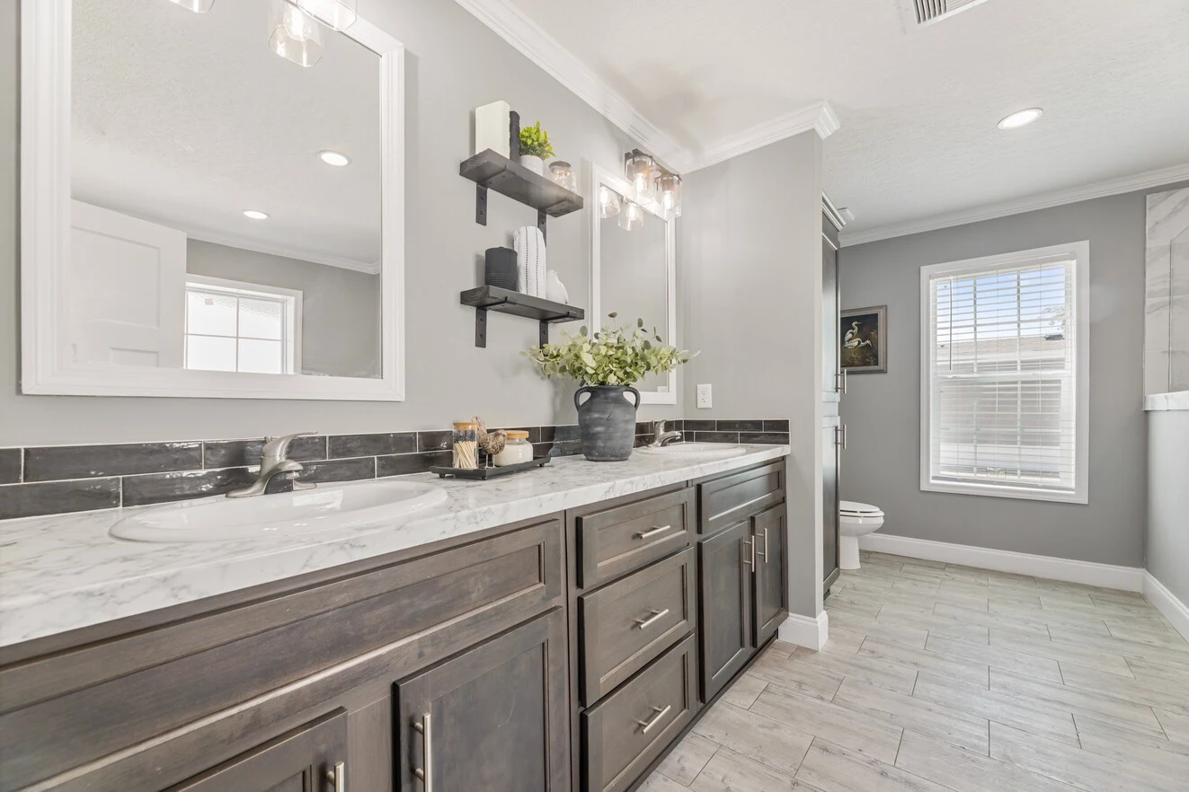 Modern bathroom with marble countertop, dark wood cabinets, double sinks, wall-mounted shelves, and a window with blinds letting in natural light.