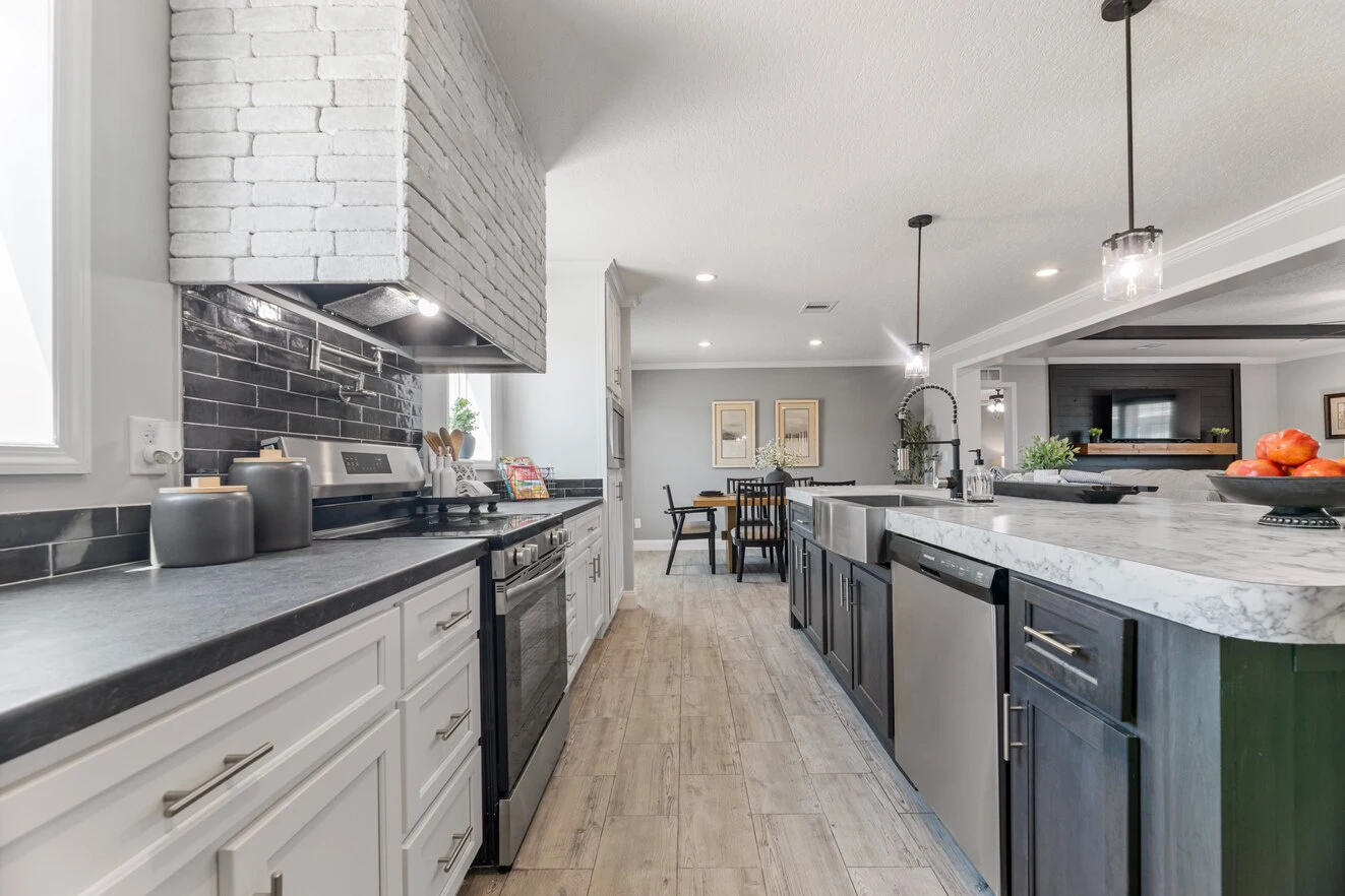 Modern kitchen with white and dark cabinetry, stainless steel appliances, marble countertops, pendant lights, and a view into a dining and living area.
