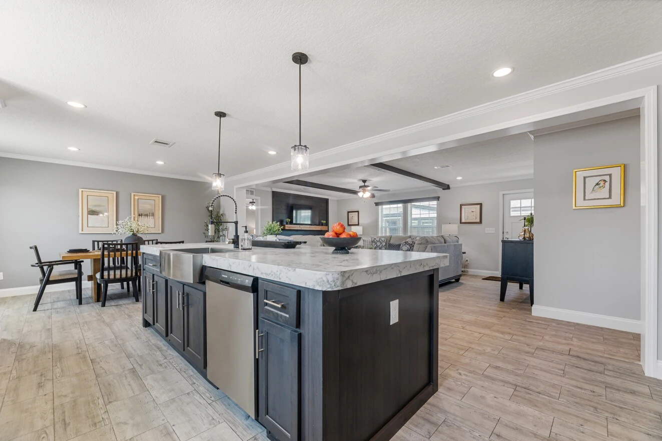 Modern open-concept kitchen with a marble island, dark cabinetry, pendant lighting, and stainless steel appliances, adjoining a dining area and living room with wood-look tile flooring.