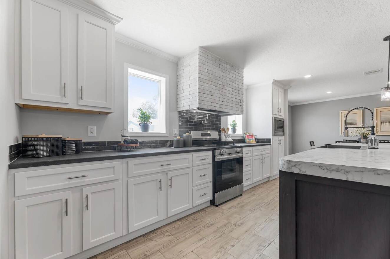 Modern kitchen with white cabinets, black countertops, stainless steel appliances, and wood-look tile flooring. Two windows provide natural light.