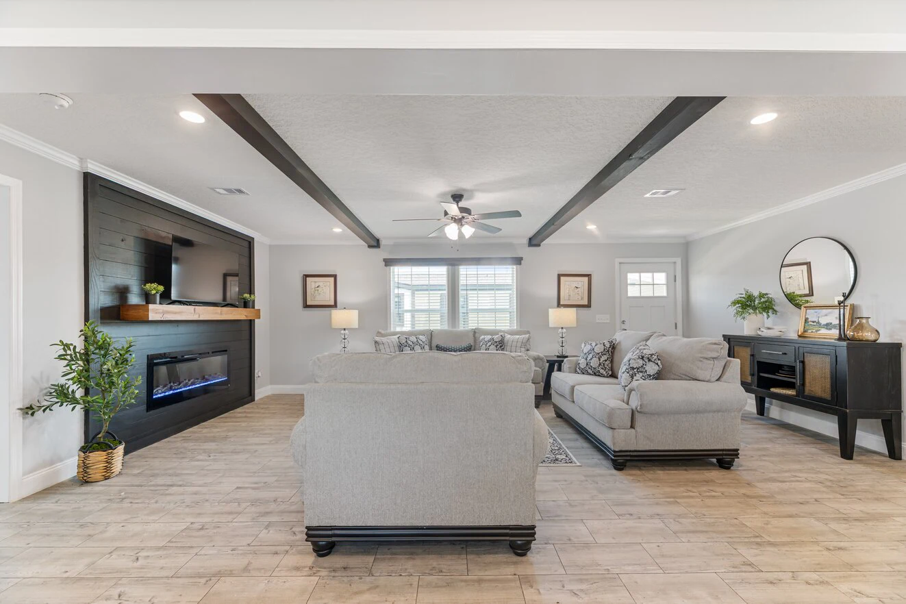 Modern living room with light wood floors, two gray sofas, a black electric fireplace with a mounted TV, and large windows letting in natural light.