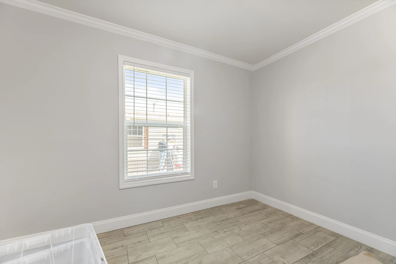 Empty room with light gray walls, white trim, wood-style tile flooring, and a window with white blinds letting in natural light.