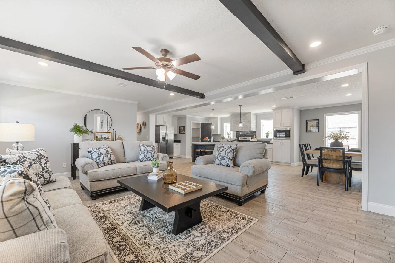 Spacious open-concept living room with neutral sofas, a coffee table, ceiling fan, visible kitchen, and dining area in a modern home.