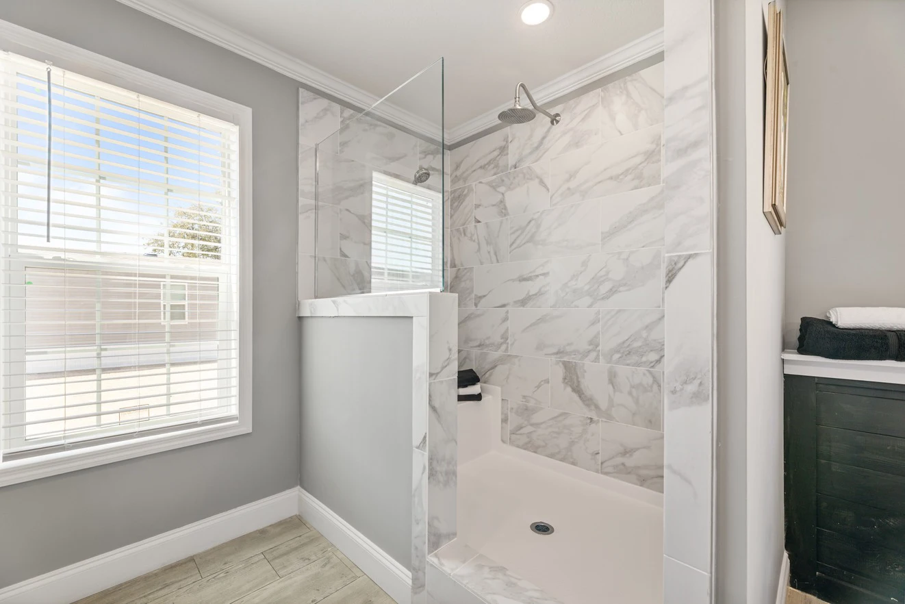A modern bathroom shower with marble tile walls, a glass partition, and a window allowing natural light into the space.