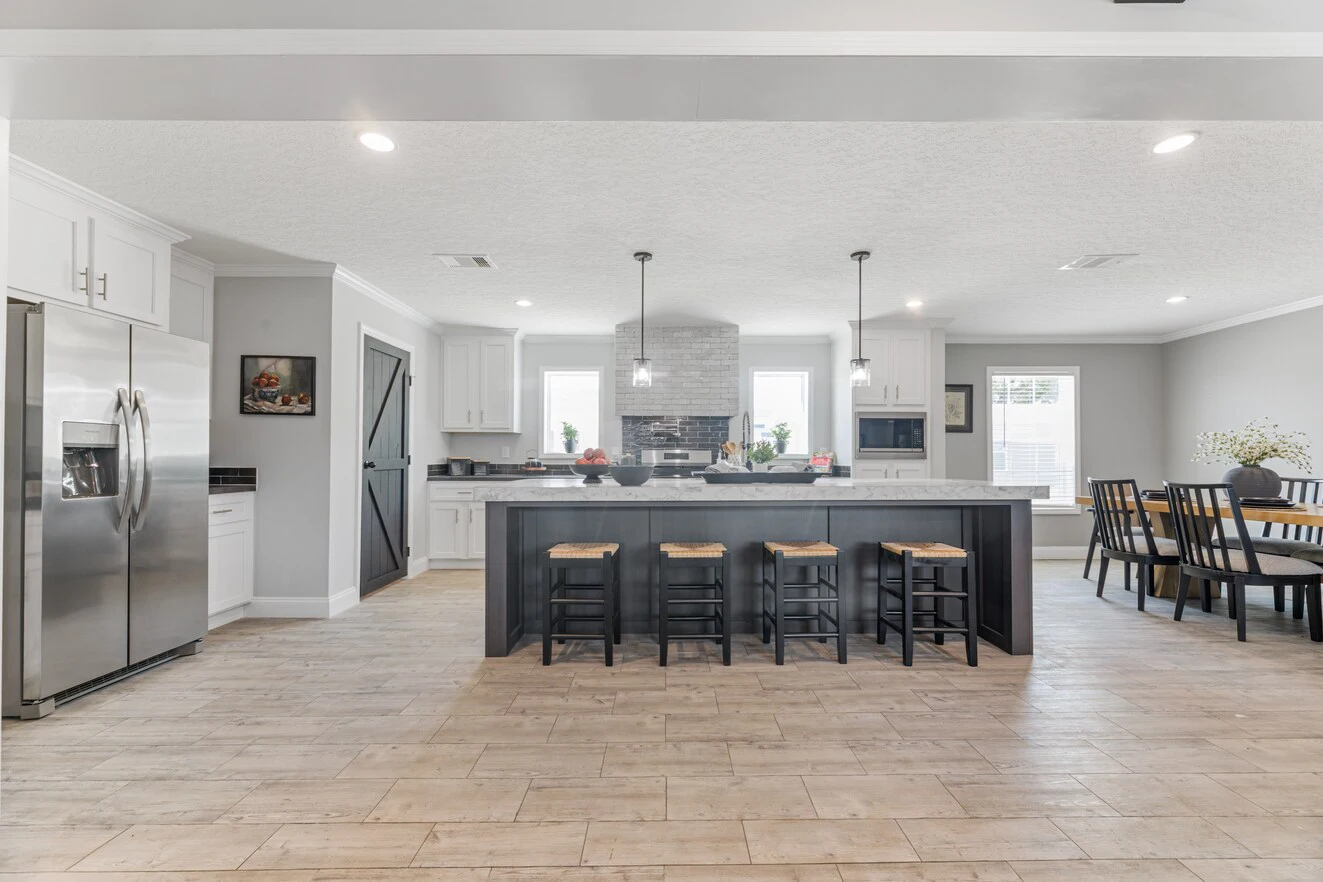 Modern kitchen with a large island, four bar stools, stainless steel appliances, white cabinetry, pendant lights, and a dining area with a table and chairs.
