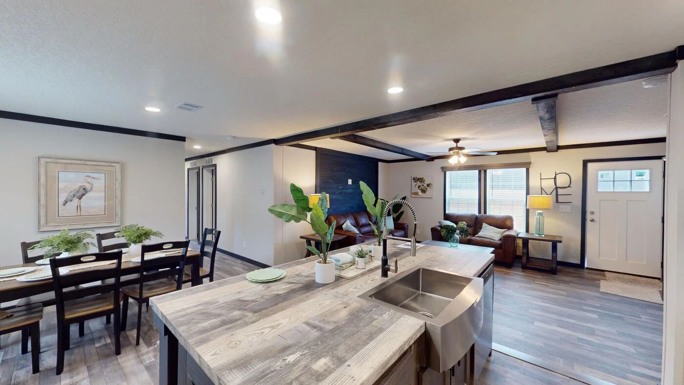 Open-concept living space with a modern kitchen island, farmhouse sink, dining area, and cozy living room with brown sofas and large windows.