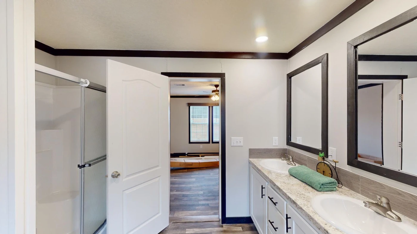 Bathroom with a double sink vanity, large mirrors, a glass shower, and an open door leading to a room with a bathtub and wood flooring.