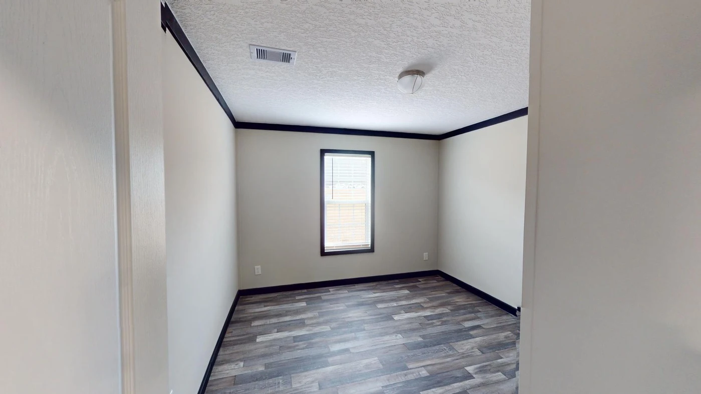 Empty room with beige walls, a single window, dark trim, and wood-look flooring. Ceiling has a light fixture and an air vent.