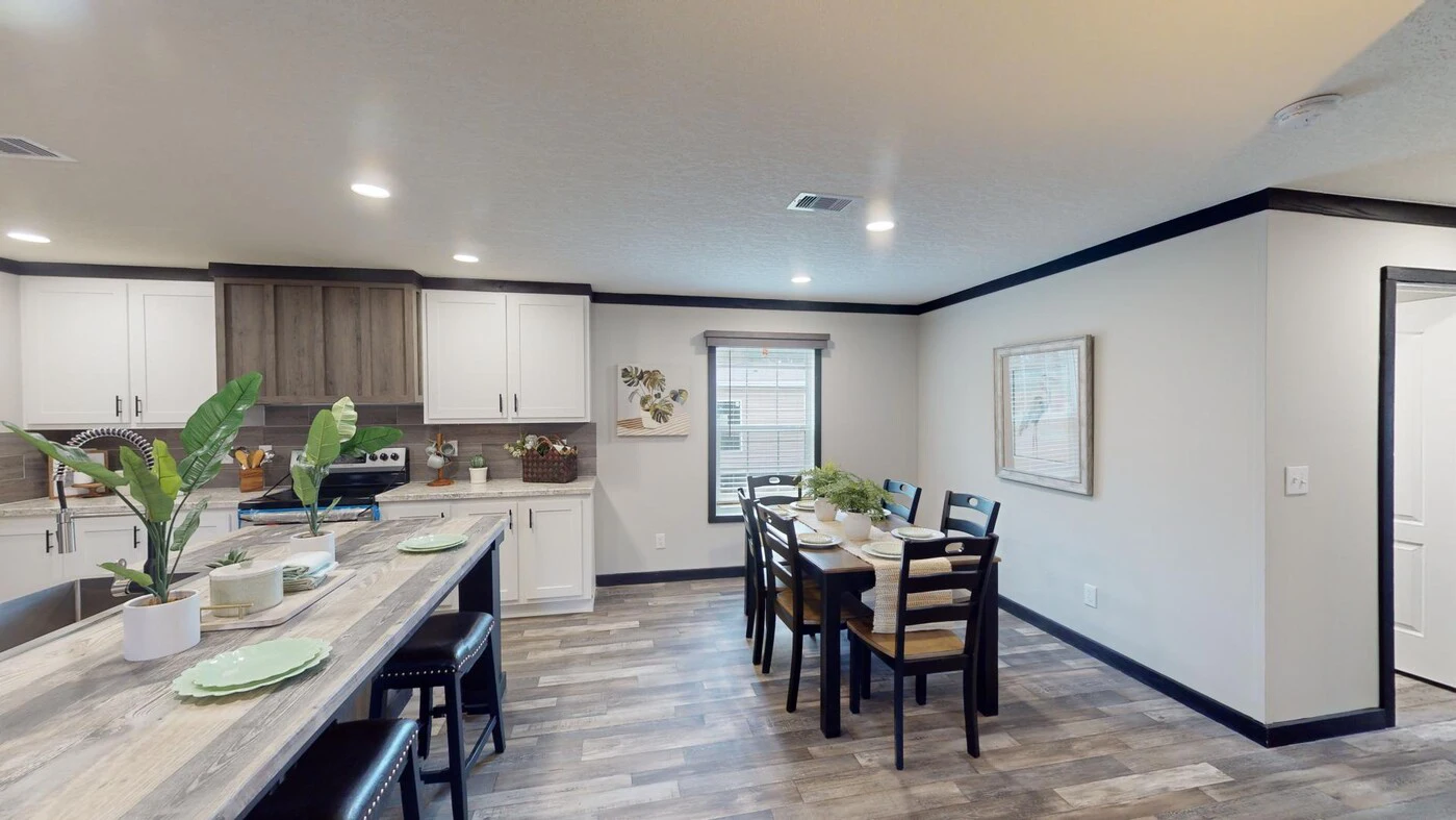 Modern kitchen and dining area with white cabinets, wood accents, a long island with bar stools, and a dining table set for six. Large window provides natural light.
