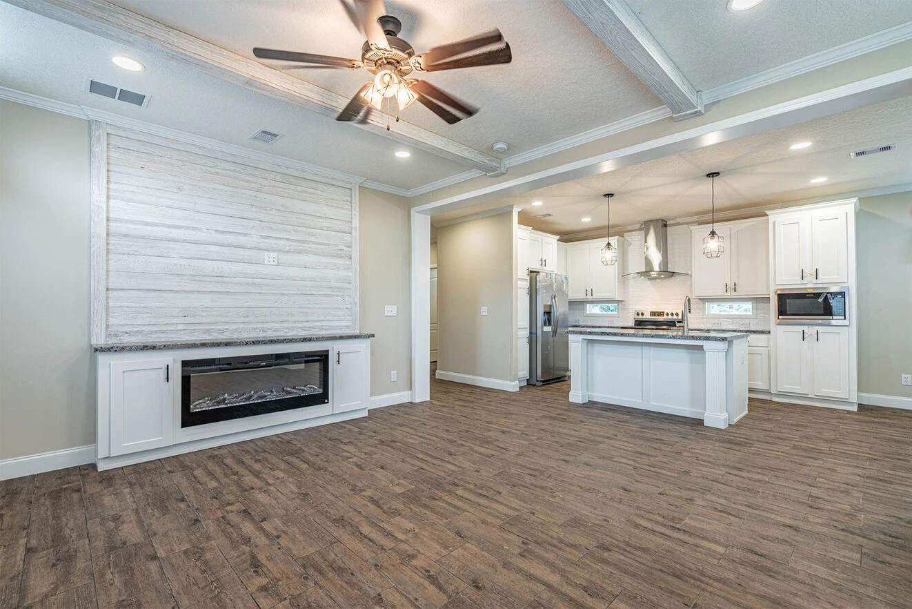 Open-concept kitchen and living area with wood flooring, white cabinets, stainless steel appliances, ceiling fan, and a wall-mounted fireplace.
