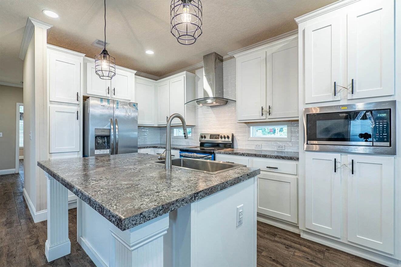 Modern kitchen with white cabinets, stainless steel appliances, a large island with a sink, and pendant lighting over a granite countertop.