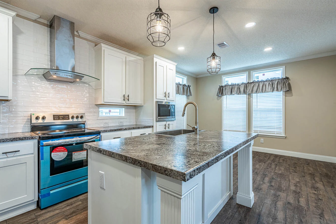 Modern kitchen with white cabinets, stainless steel appliances, large granite island with sink, pendant lights, and wood flooring.