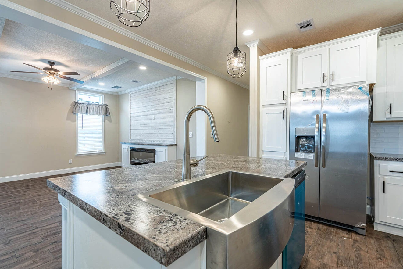 Modern kitchen with stainless steel appliances, farmhouse sink, granite countertops, and an open layout connecting to the living room with ceiling fan and large window.