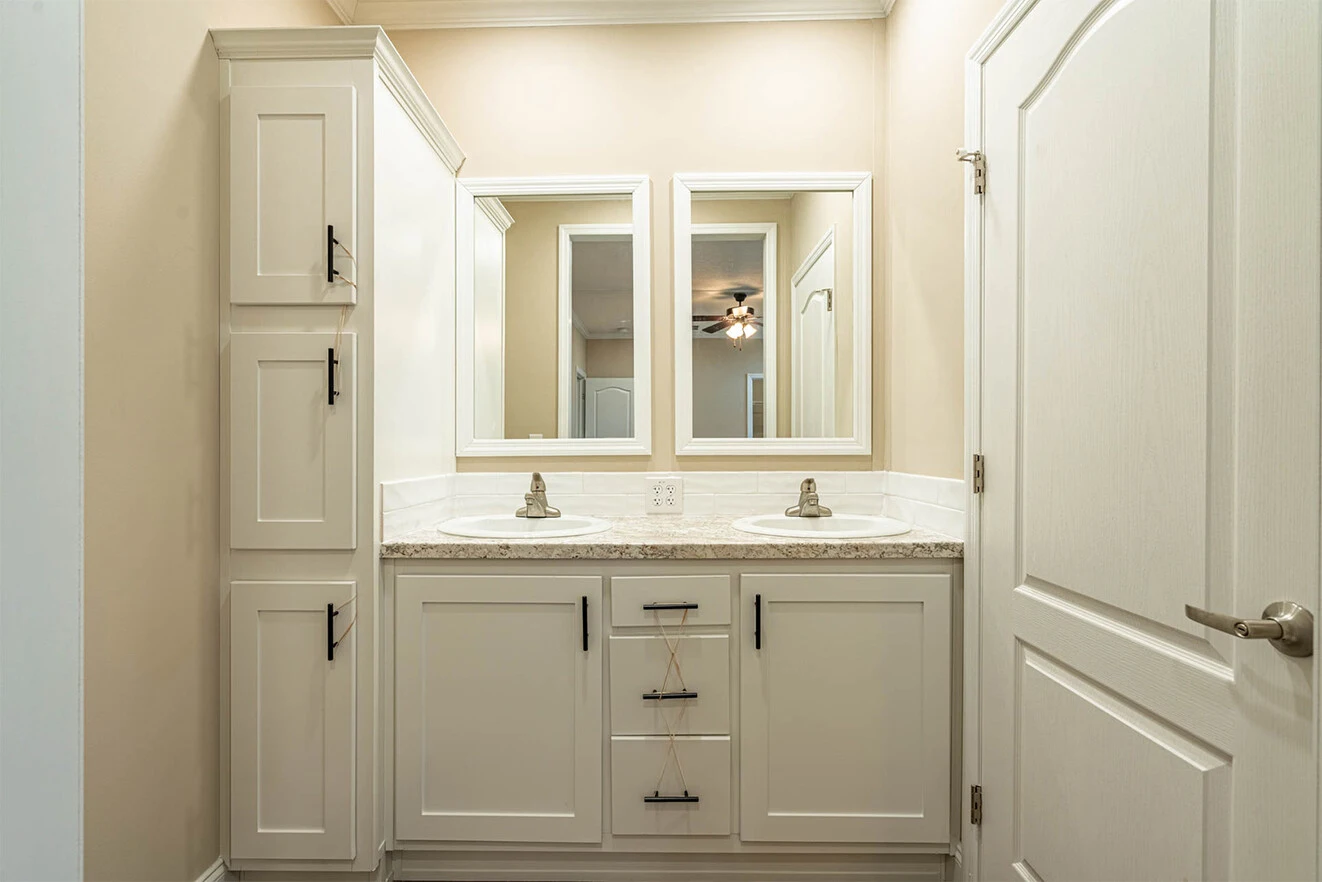 Double sink bathroom vanity with white cabinets, two mirrors, silver faucets, and a neutral color scheme. A closed door is visible on the right side of the image.