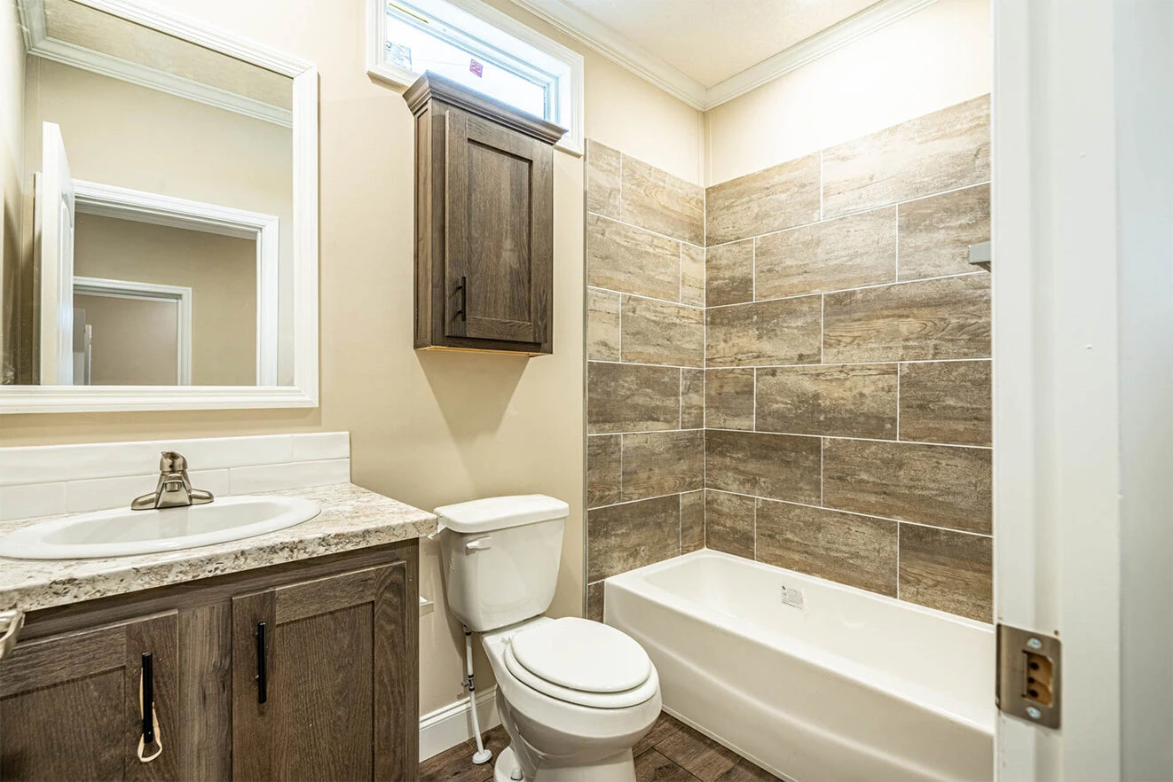 A bathroom with a sink and cabinet, a toilet, and a bathtub with brown tile surround; a wall cabinet is mounted above the toilet.