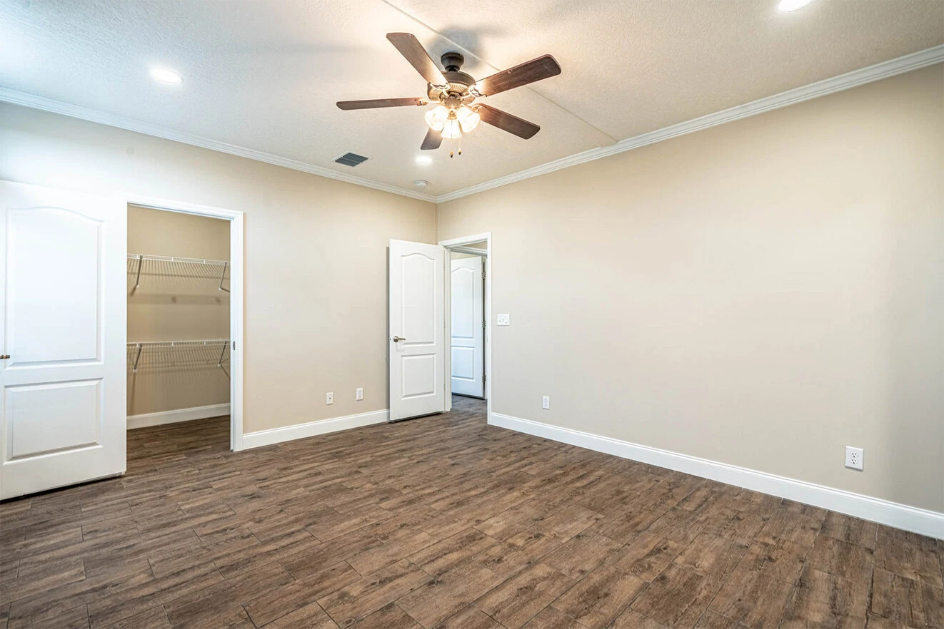 Empty room with wood-style flooring, beige walls, ceiling fan with lights, two open white doors, and a walk-in closet with wire shelving.