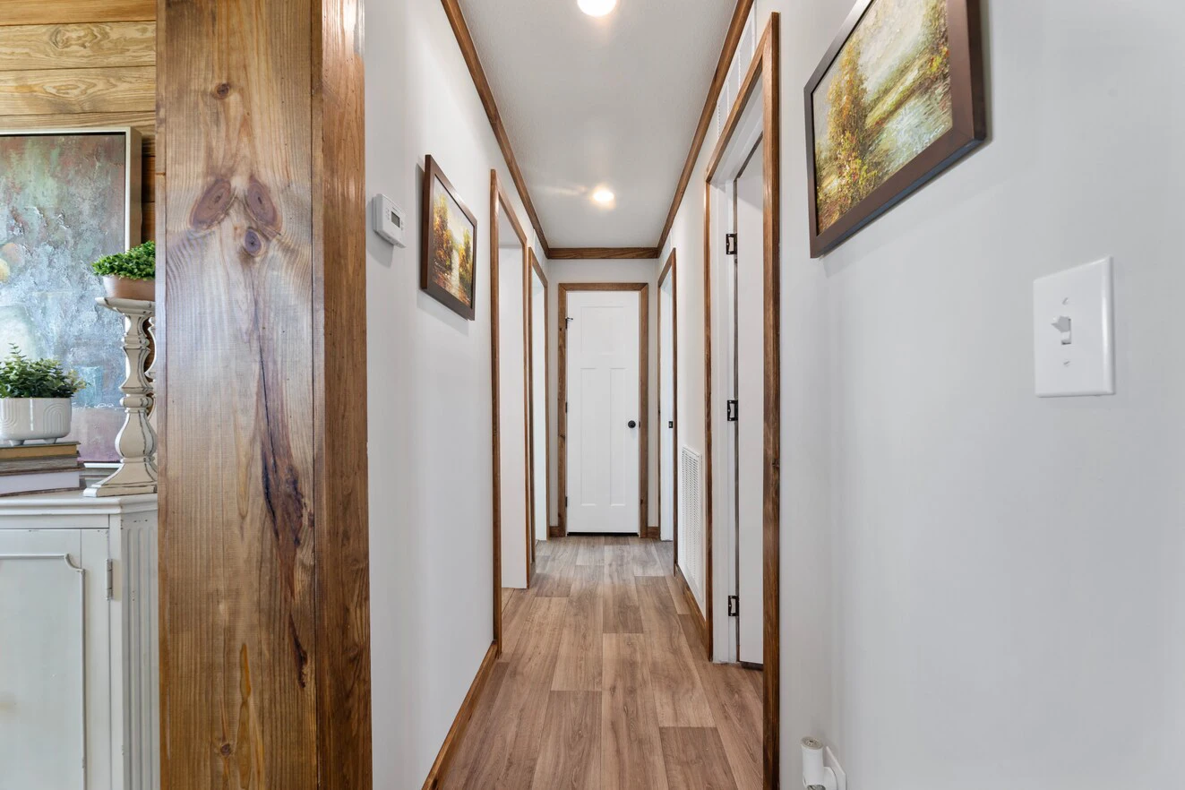 A hallway with wood trim and flooring, white walls, several closed doors, framed artwork, and ceiling lights.