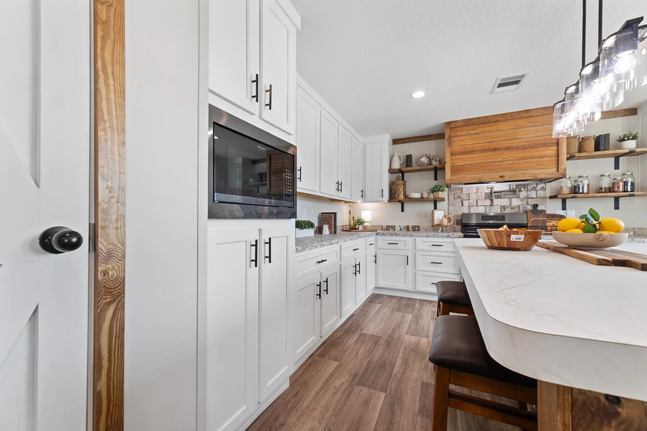 Modern kitchen with white cabinets, wood accents, open shelves, a built-in microwave, and a central island with stools and a bowl of lemons.