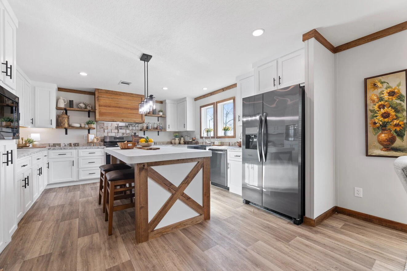 Modern kitchen with white cabinets, stainless steel appliances, a central island with wood accents, and sunflower artwork on the wall. Light wood flooring and recessed lighting throughout.