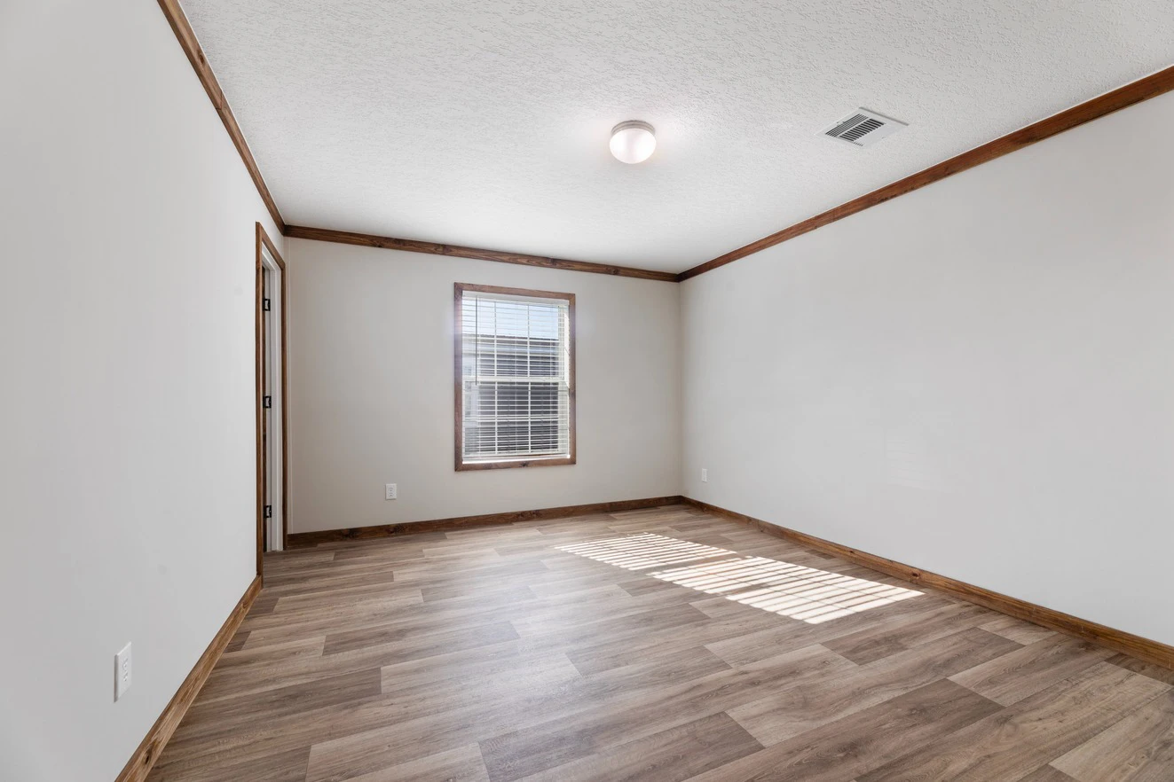 Empty room with light-colored walls, wood trim, vinyl plank flooring, a single window with blinds, and a ceiling light.