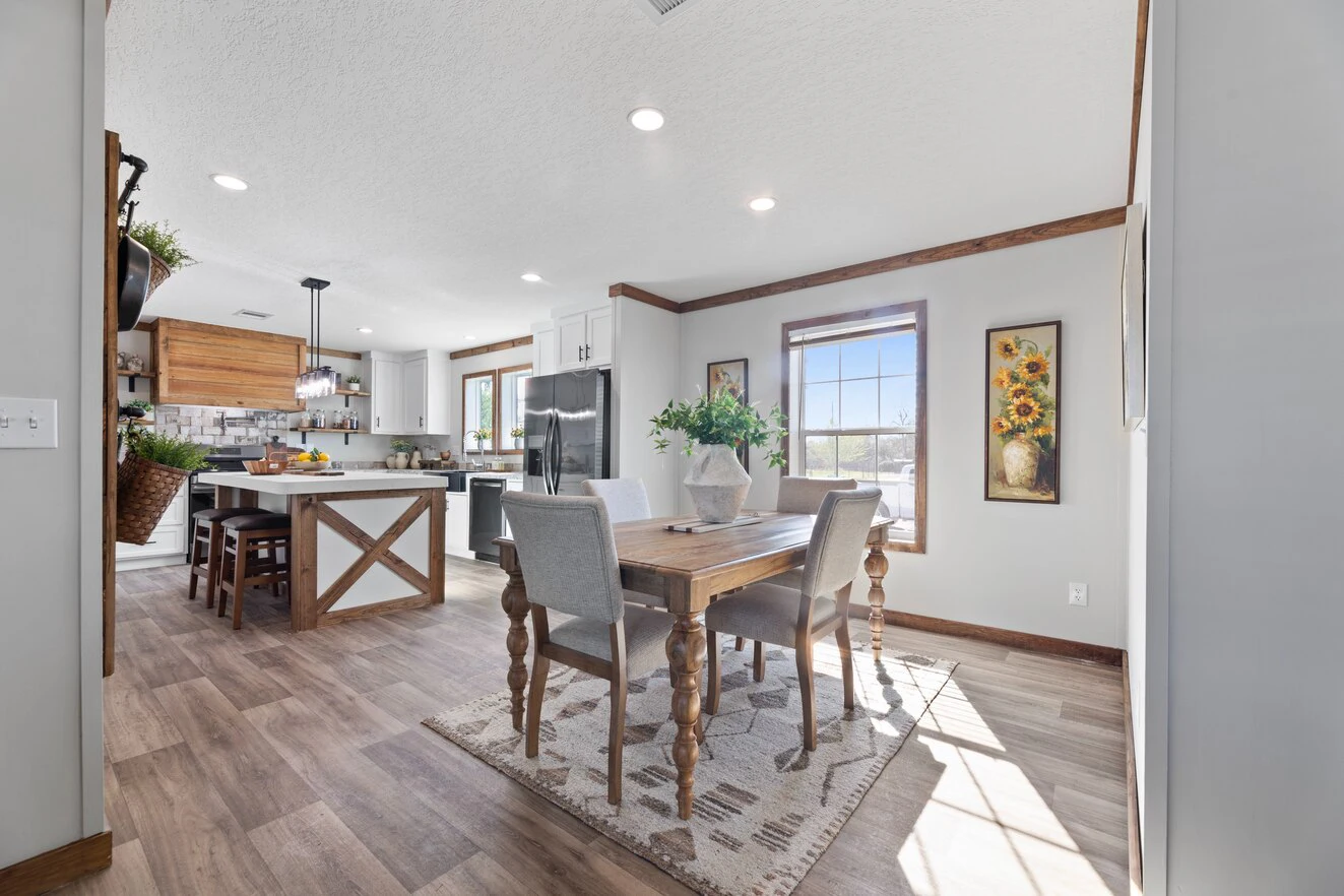 Bright kitchen and dining area with wooden floors, a wooden dining table with four chairs, stainless steel appliances, and large windows letting in natural light.