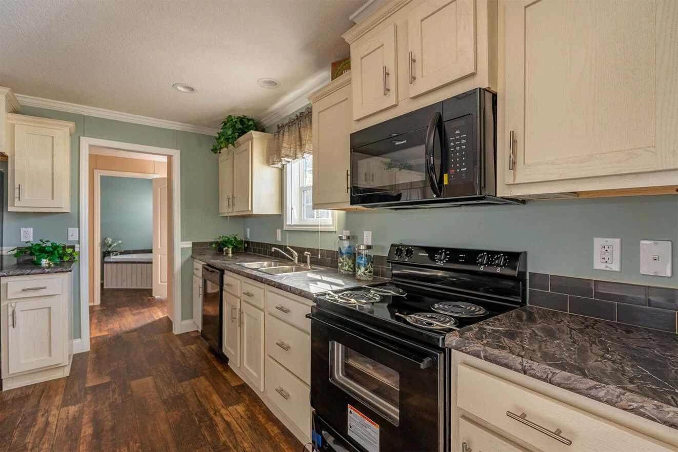 te28523c_14_1713813631672_1323_12 Modern kitchen with white cabinets, black appliances, marble countertops, wood flooring, and plants above cabinets. Natural light enters through a window above the sink.